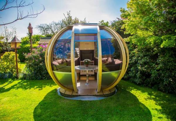 garden pods - photo of a garden pod with glass walls, seater and table in a backgarden.